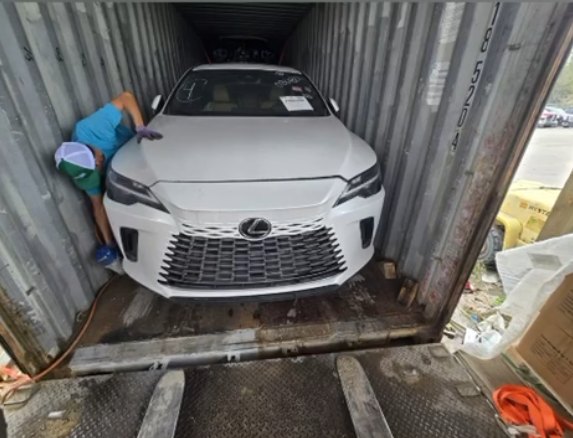 Biały Lexus wjeżdżający do kontenera, pracownik zabezpiecza auto